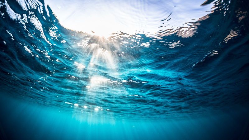 Das Foto zeigt die Unterwasseraufnahme der Meeresoberfläche mit Sonnenstrahlen und Wellen.