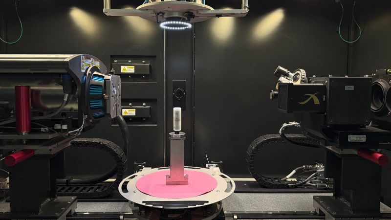 Das Bild zeigt eine Schlacke-Probe in einem Zylinder auf einem Probenhalter zwischen Röntgenquelle und Detektor im Inneren eines Röntgen-Computertomographen.