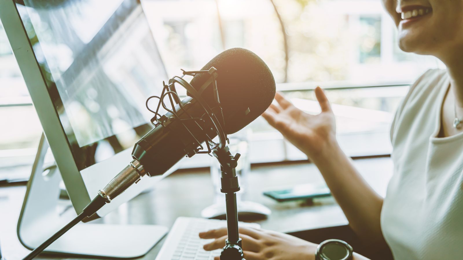 Das Bild zeigt eine Frau vor einem Mikrofon an einem Computer.