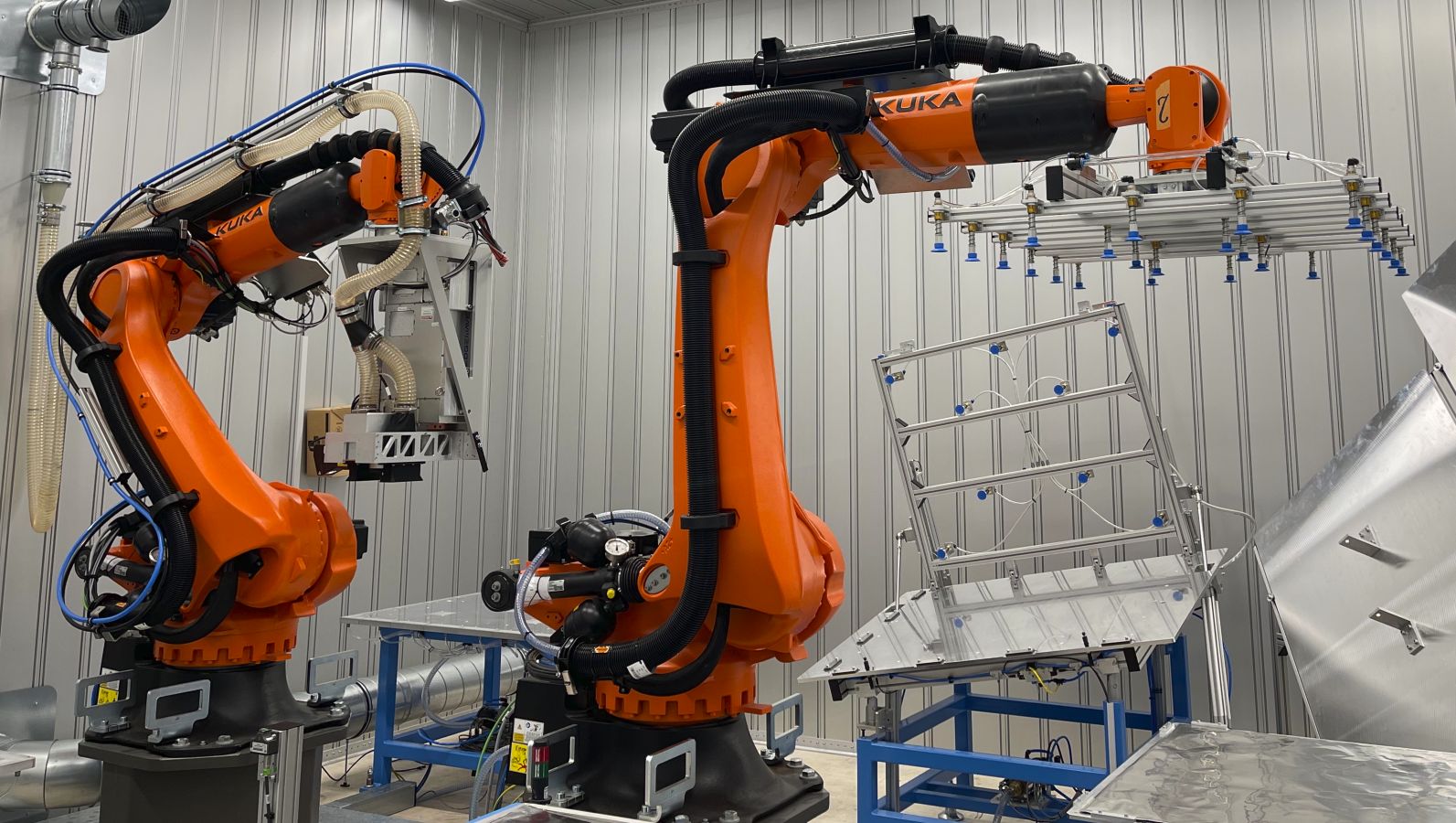 Das Bild zeigt die Musterfertigungsstrecke für Elektrolyseure. In einer silberfarbenen Metallkabine, ähnlich einer Garage, findet die Laservorbehandlung von Metallbauteilen statt.