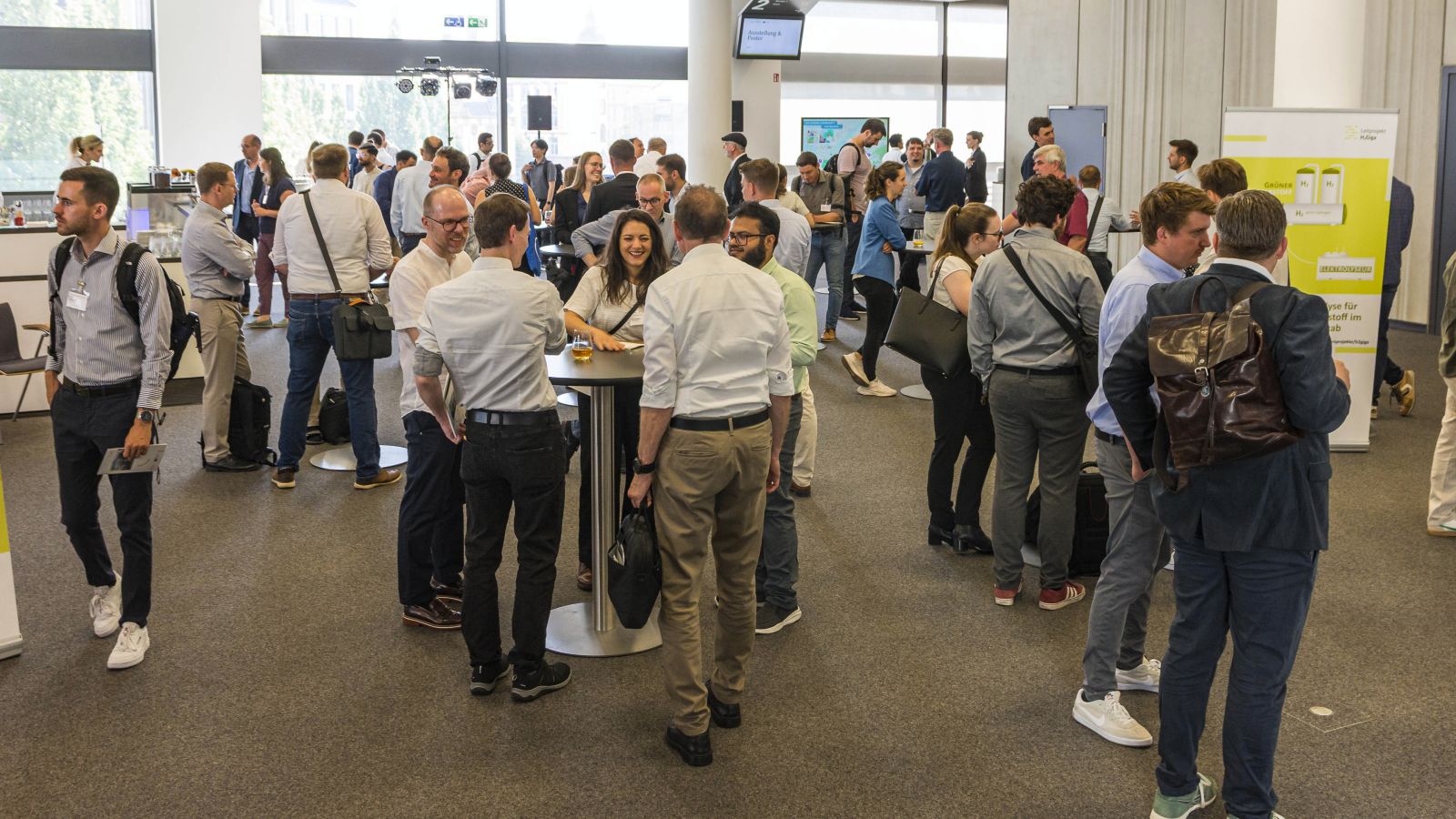 Auf dem Foto sieht man sich unterhaltende Personen an Stehtischen im Vorraum eines Konferenzraumes.